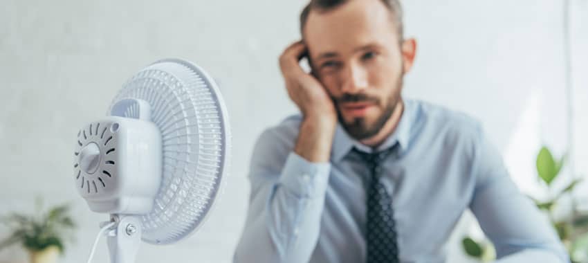 Man in nice shirt and tie sits in front of blowing fan to cool off.