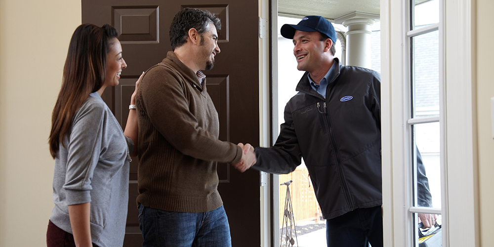 HVAC tech in hat and jacket greets homeowners before furnace maintenance services.