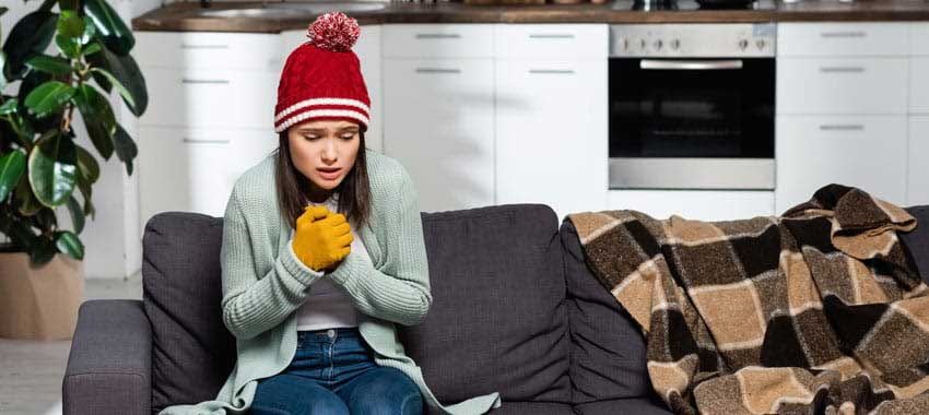 Young woman shivering on couch after furnace stops working.